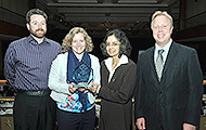 Photo of two men and two women posing for a group picture. One of the women is holding an award.