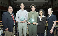 Photo of five men and one woman posing for a group picture. Three of the men are holding awards.