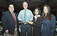 Photo of two men and two women posing for a group picture. One of the men is holding an award.