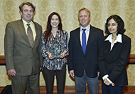 Photo of two women and two men posing for a group picture. The woman in the center is holding an award.