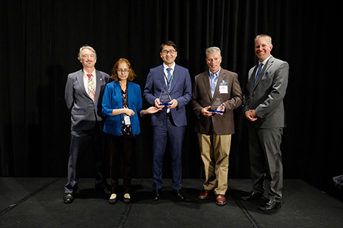 Five people stand with two award trophies.