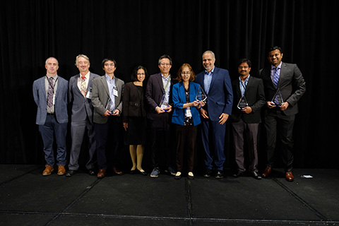 Nine people stand with five award trophies.