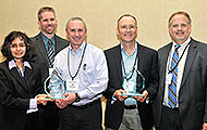 Photo of four men and one woman posing for a group picture. Two of the men are holding awards.