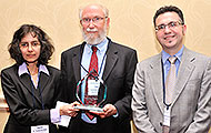 Photo of two men and a woman posing for a group picture. One of the men is holding an award.